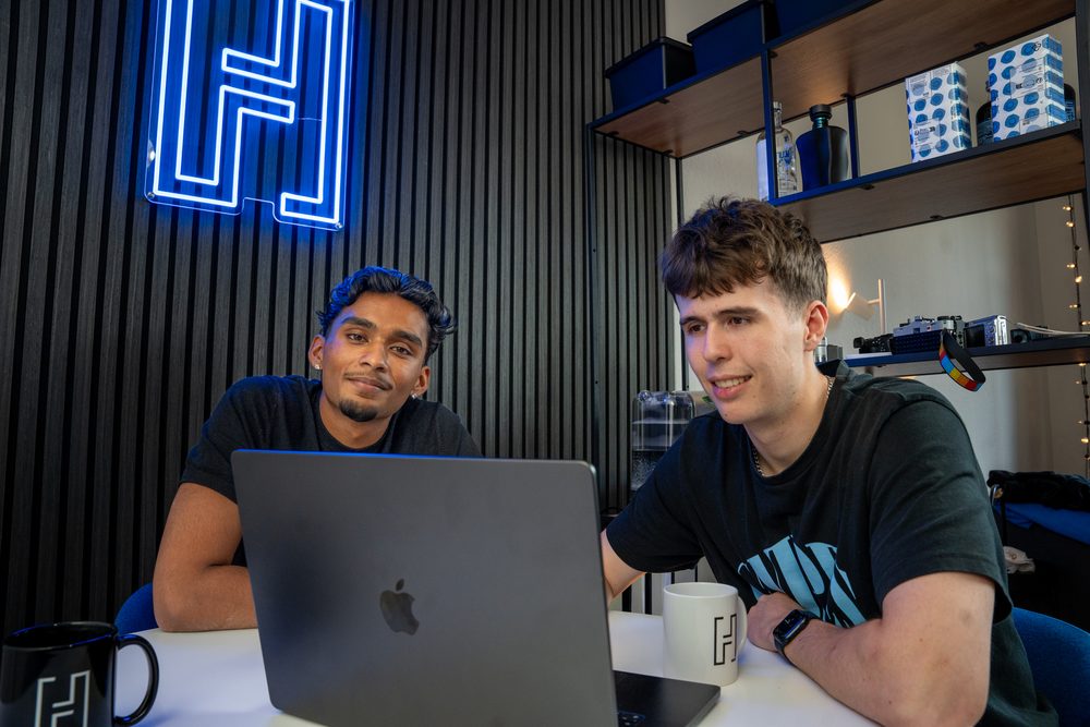 Rojith Ragavan und Janis Chatelain am Laptop vor dem Haldelain-Neonlogo